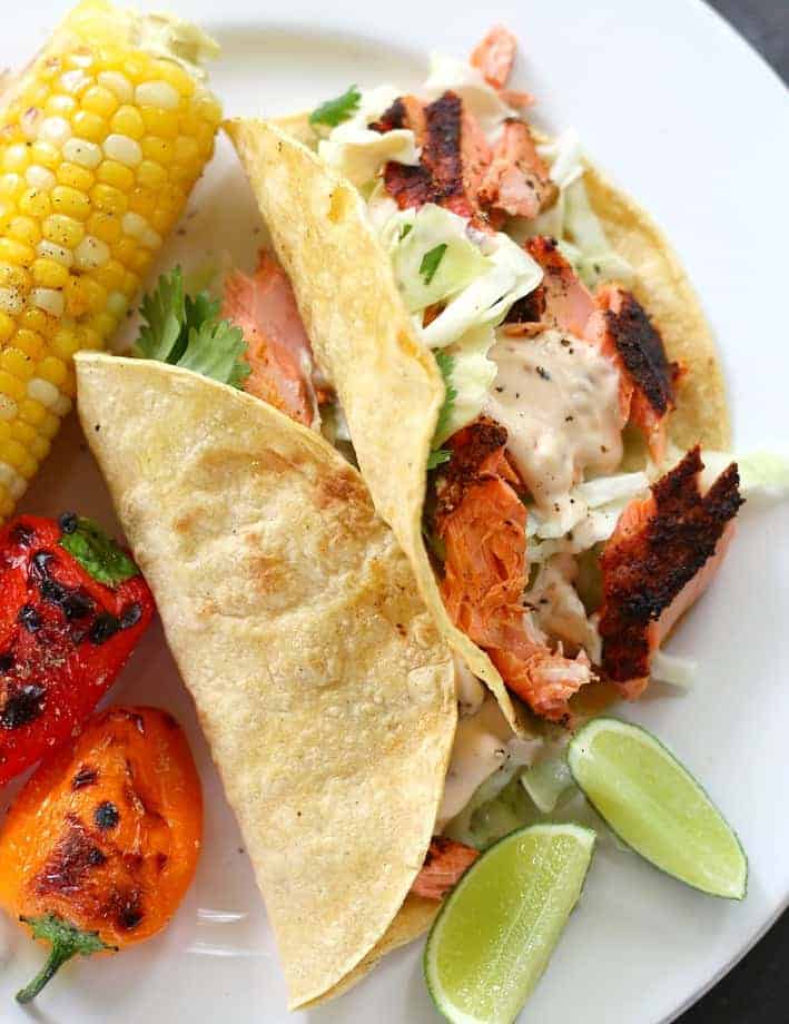 grilled salmon tacos on a plate served with corn one the cob and grilled peppers