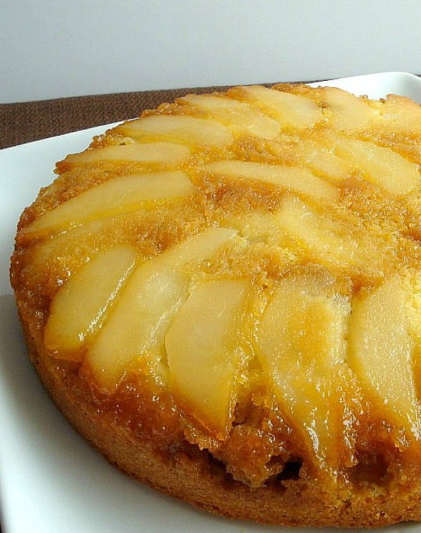 Upside down pear cake before cutting on white plate.