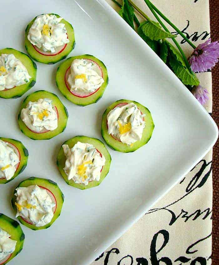 Cucumber slices with herbed cream cheese and sliced radishes on a white plate