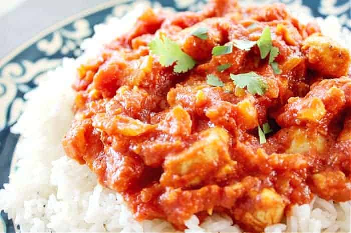 Close up of butter chicken on rice on white and blue plate