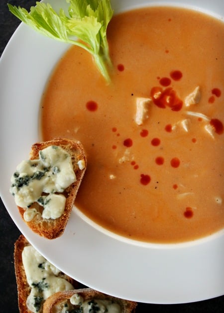Buffalo Chicken Soup in white bowl with crusty bread, blue cheese on edge. Celery in bowl.