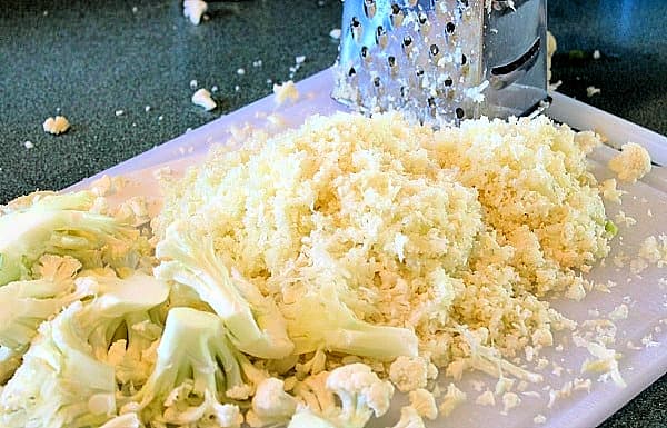 cauliflower with partially grated cauliflower on a white plate with grater.
