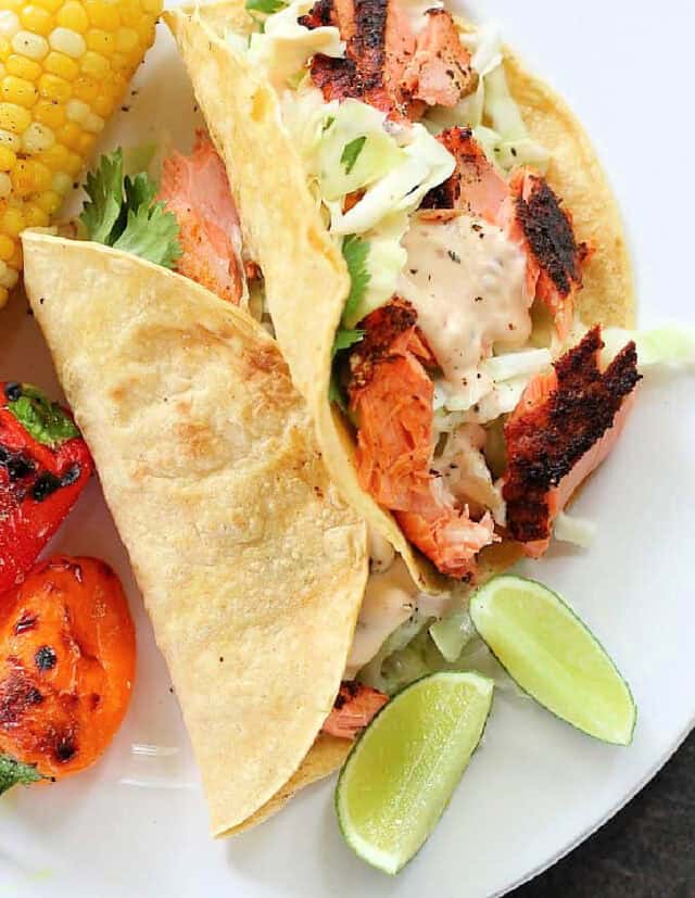 Two grilled fish tacos with lime wedges.