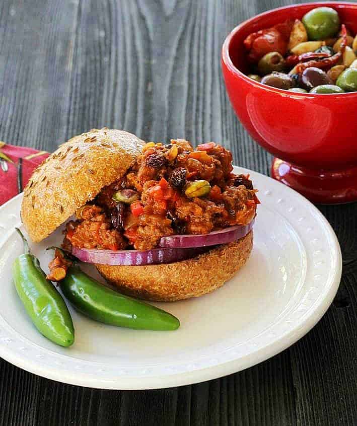 Bombay sloppy joes with Serrano peppers on white plate, olives in red bowl
