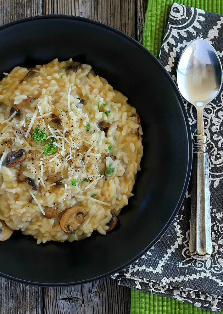 Mushroom risotto in a black bowl with a spoon on the side