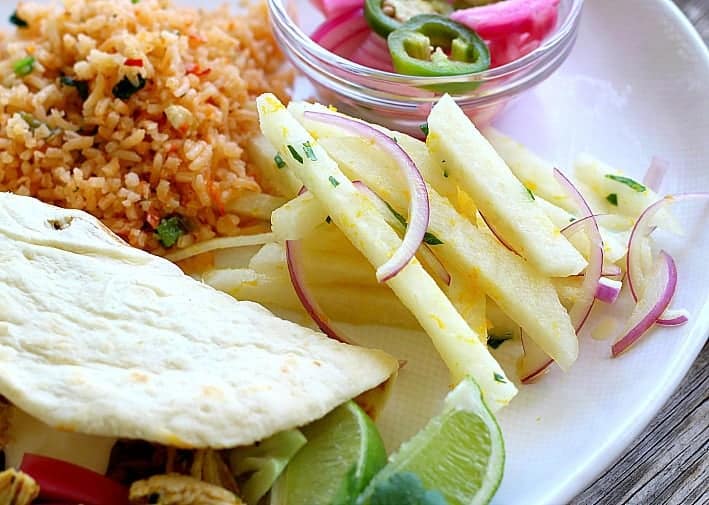 Jicama on a plate served with rice, a taco and pickles onions 