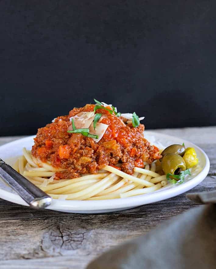 Bolognese on a white plate with spaghetti served with green olives