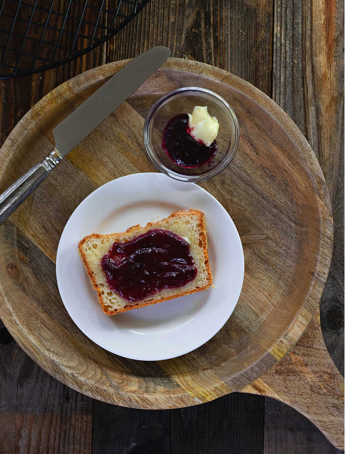 One slice on a white plate with jam. Jam and butter on the side in a small glass dish