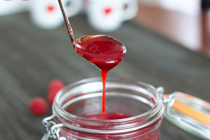 raspberry puree on a spoon pouring into a clear jar