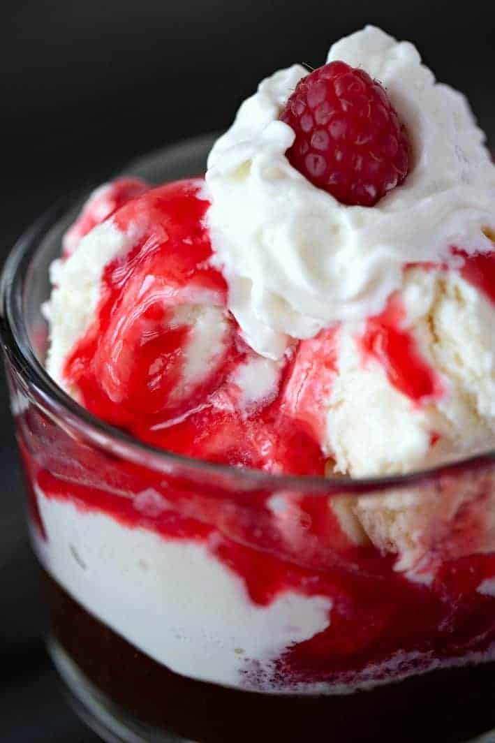 raspberry puree on ice cream with whipped cream and a raspberry in a clear bowl
