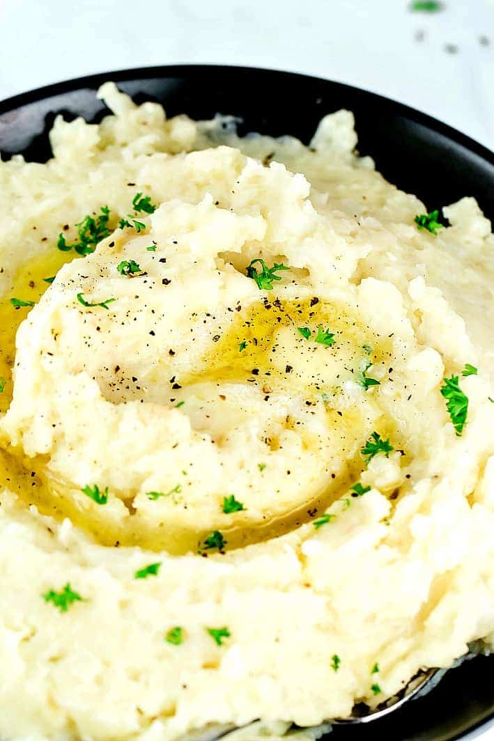 Mashed cauliflower and potatoes swirled with butter and parsley on top in a black bowl