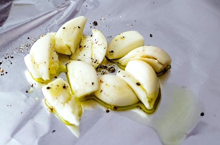 Garlic cloves with salt and pepper on tin foil before roasting