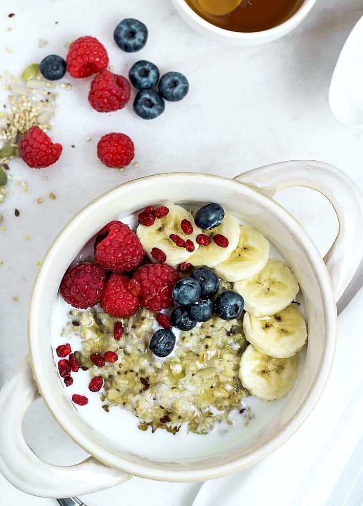 Porridge topped with berries and bananas served in a white bowl 