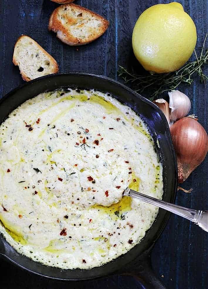 baked ricotta in a cast iron skillet. toasted bread, shallots and lemon on blue wood table