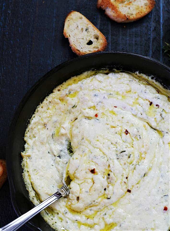 baked ricotta in a cast iron skillet with a spoon. crouton bread on blue wood table