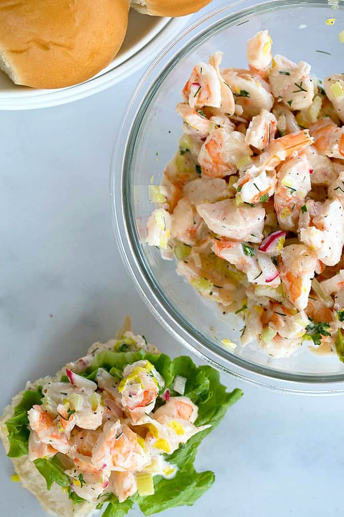 Shrimp salad in a glass bowl with some on a roll with lettuce on the side
