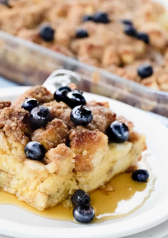 French Toast Casserole slice topped with blueberries, syrup served on a white plate