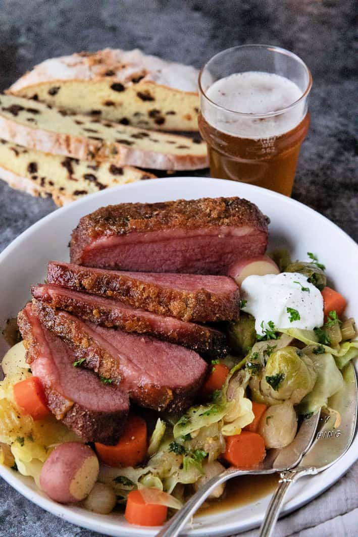 Emerald Isle Corned Beef sliced with vegetables on white plate served with Irish soda bread and beer