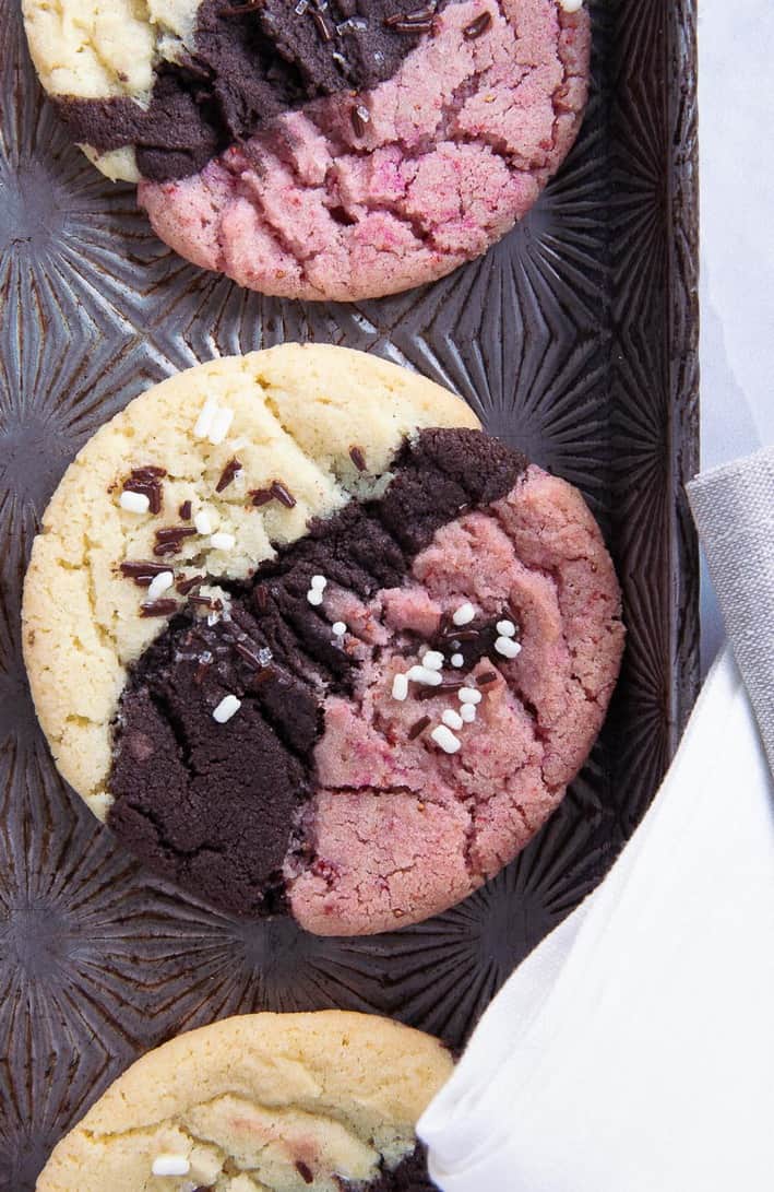 close up of three neapolitan cookies on a baking sheet with napkins to the bottom right