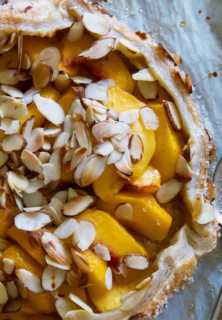 Close up view of peach puff pastry tart with sliced almonds