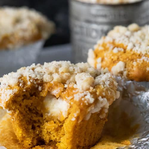 close up of pumpkin cream cheese muffin with bite taken out of it. muffins in the back with baking tin. streusel on top