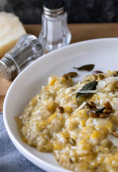 pumpkin risotto in white dish with salt and pepper shakers at top. crisp sage leaves and pumpkin seeds on risotto