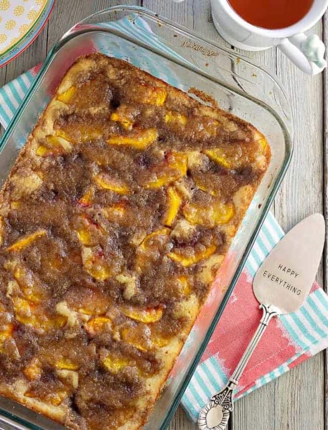 Peach kuchen in a clear baking dish. Serving spoon on side with Happy Everything written on it