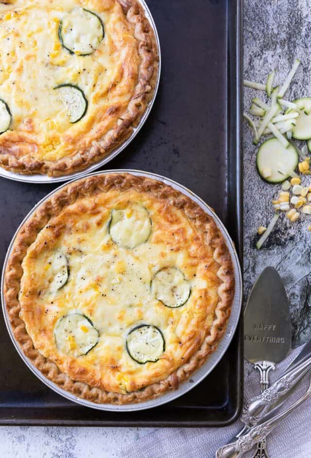 Two quiche on a baking dish with ingredients to the side