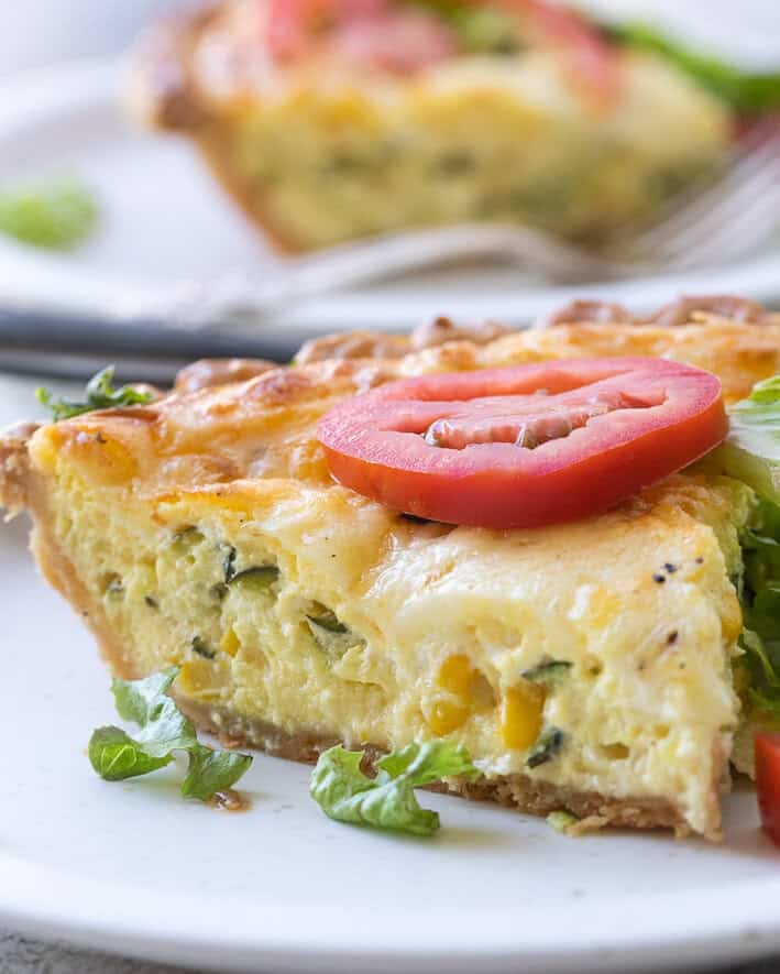 Sliced Zucchini Quiche with Monterey Jack on a plate with fresh tomato slice.