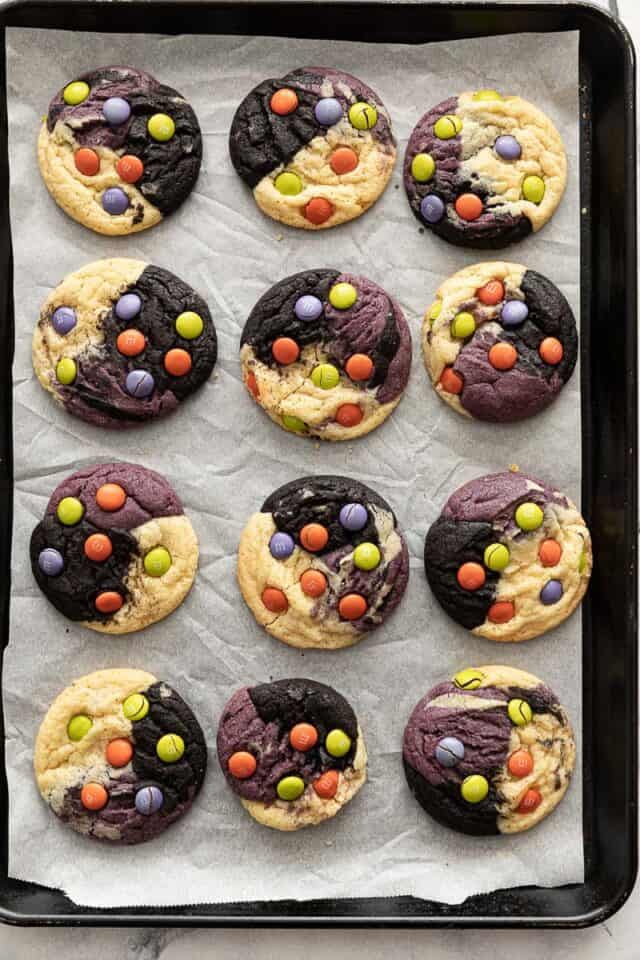 Halloween neapolitan cookies layered on parchment on cookie sheet. Cookies are purple black and natural with M&M's on them.