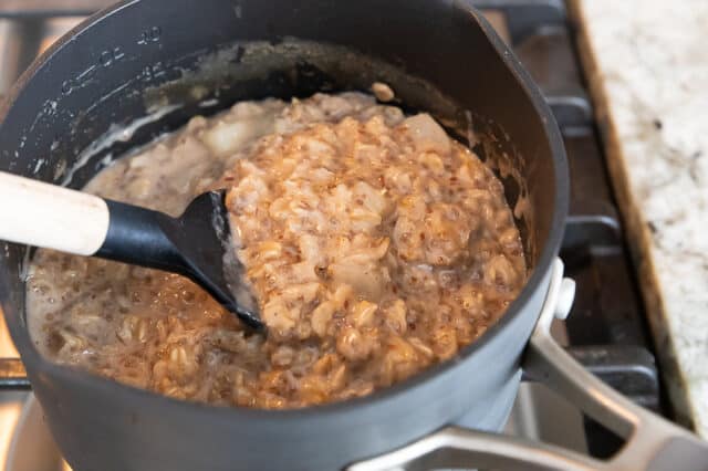 spiced pear oatmeal with spoon on top of stove, thickened after cooking.