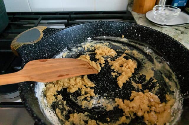 Flour and truffle butter being cooked in pan on stove. Wooden spatula stirring mixture.