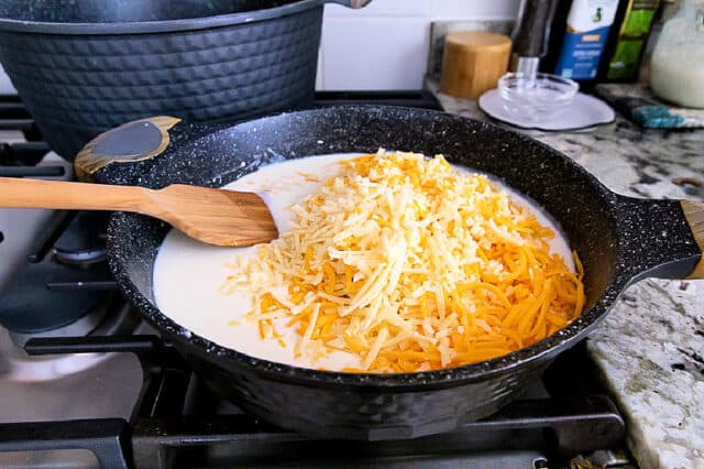 Gruyere and cheddar cheeses being added to white sauce in pan.