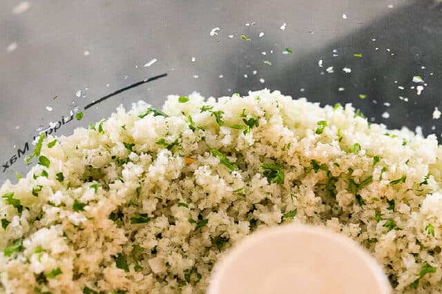 Closeup of bread crumbs, parsley and garlic in bowl of food processor