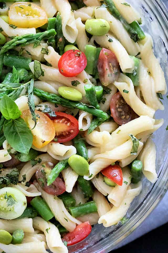 close up of pasta salad with tomatoes, edamame, pasta, asparagus, green beans, basil.