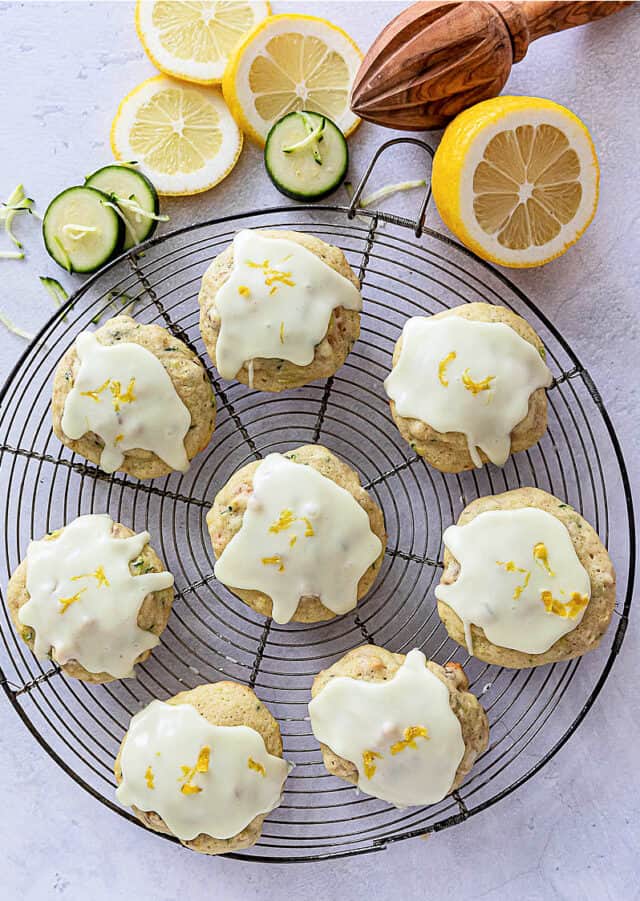 Lemon Zucchini Cookies with glaze on a cooling rack with sliced lemons with lemon juicer and zucchini slices