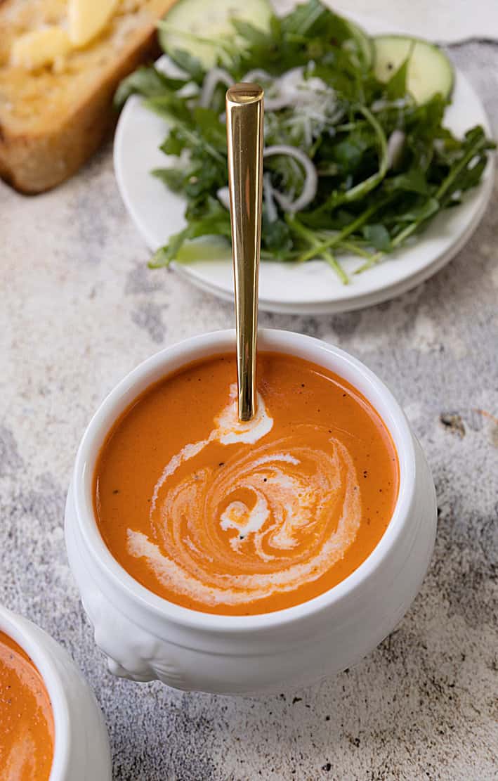 Orange tomato bisque soup with spoon. salad and bread at top