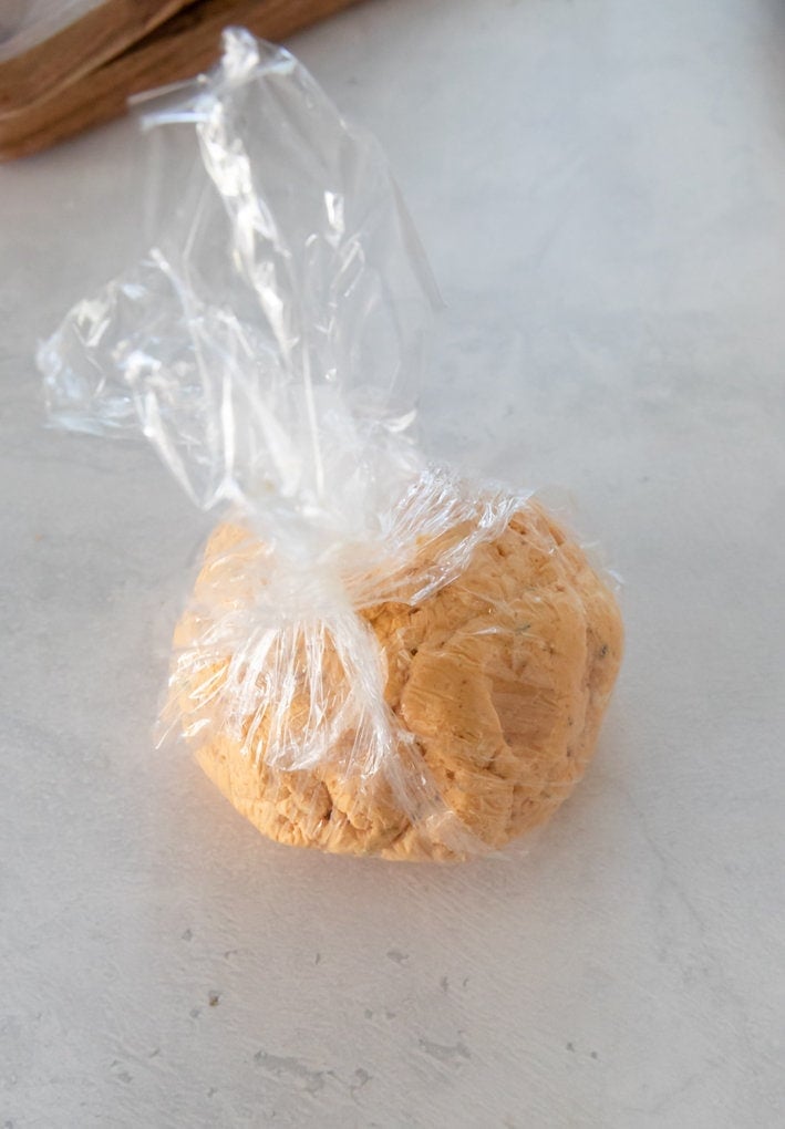 cheese ball wrapped in plastic before rolling in cheddar