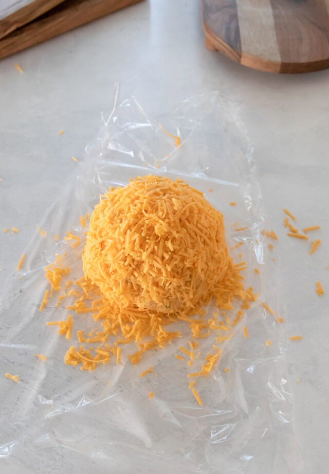 Pumpkin cheddar cheese ball covered in grated cheese.