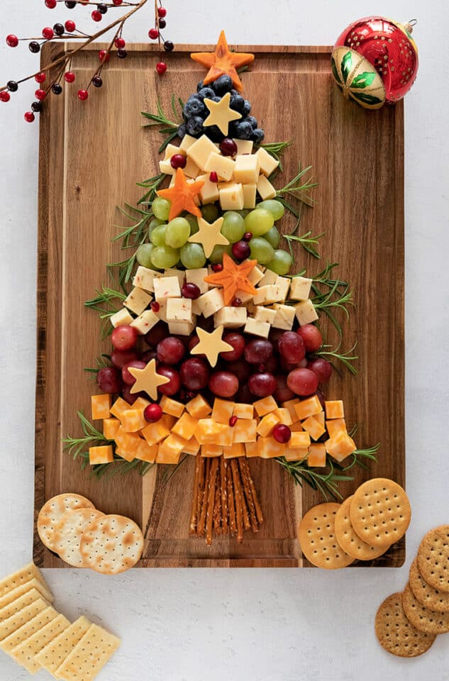 Christmas Tree Chacuterie with from top, blueberries, swiss cheese, green grapes, pepper jack cheese, red grapes, colby jack cheese. Star shaped persimmons on tree. Crackers at bottom. Ornaments at top. 