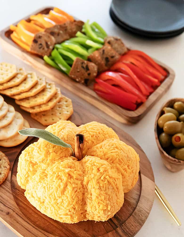 Pumpkin Cheddar Cheese Ball on serving platter with crackers, vegetables on platter in back.