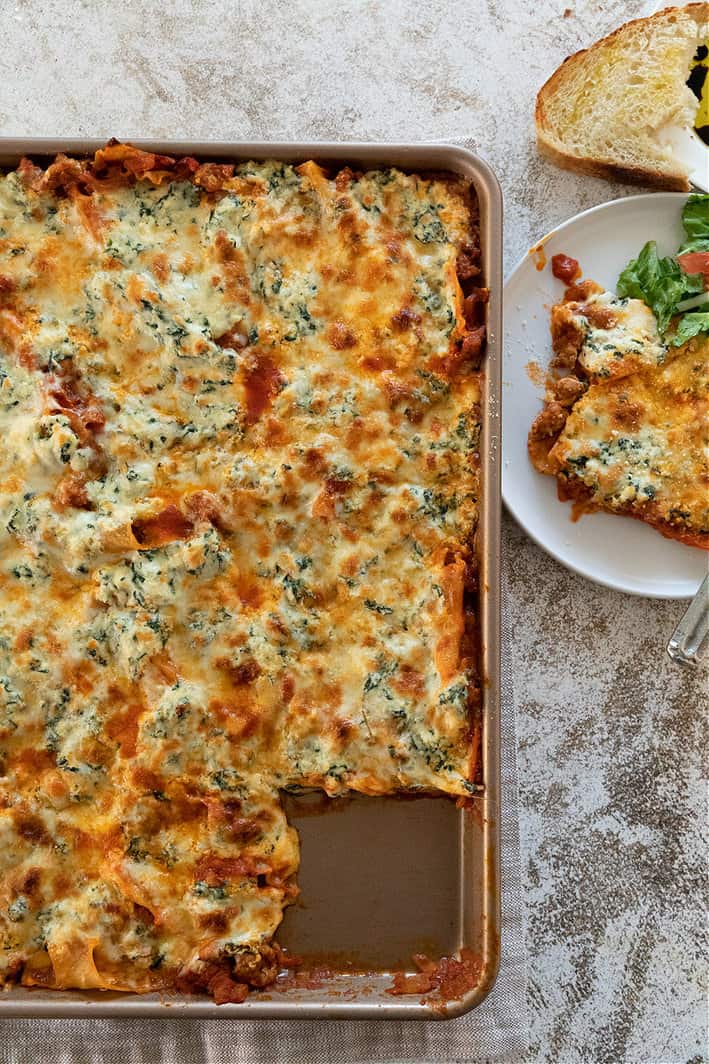Sheet pan lasagna with individual piece to side and bread at top