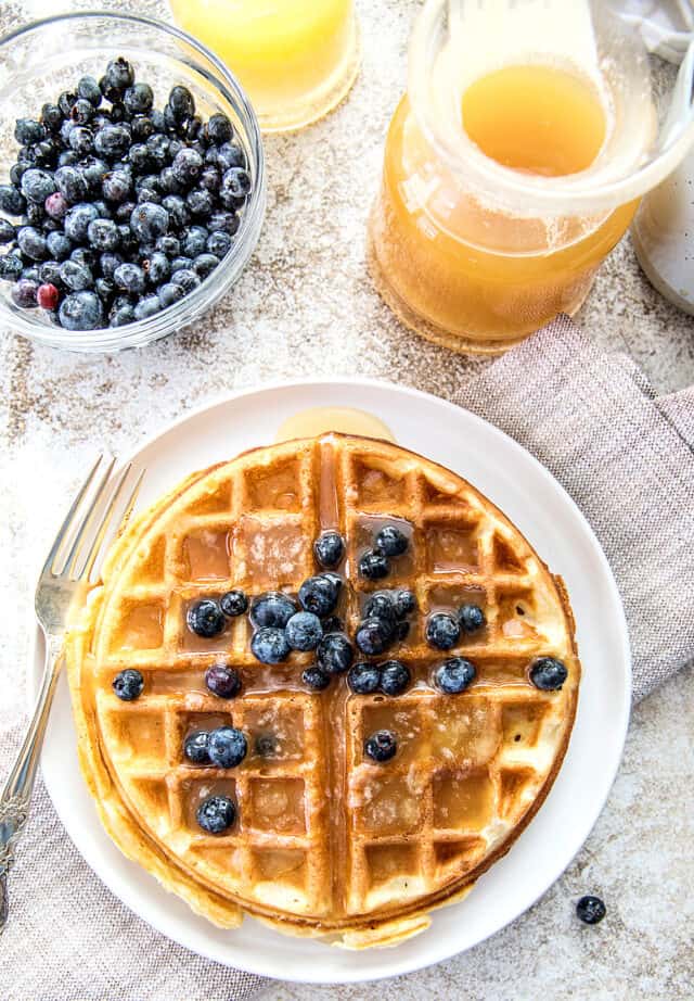 Blueberries in bowl, buttermilk syrup in glass jar and waffles with blueberries and syrup.