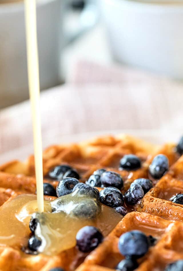 Waffle with blueberries. Buttermilk syrup is being poured over waffle
