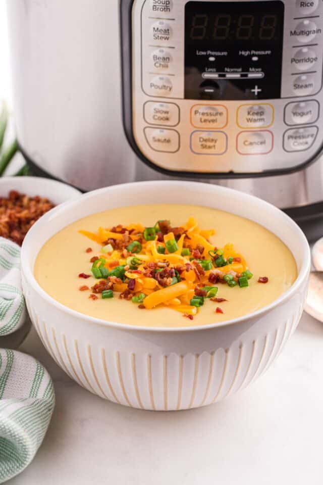 Creamy Instant Pot baked potato soup with cheddar, scallions, and bacon on top. Instant Pot in background.
