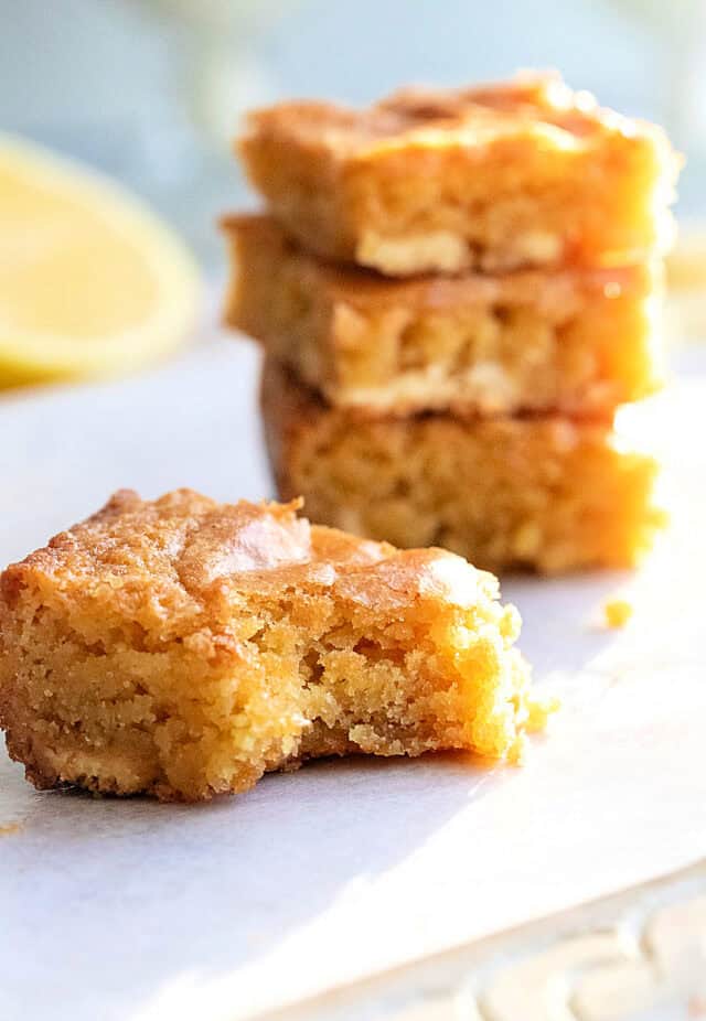Lemon Blondies stacked in back with single blondie with bite out of it in foreground.