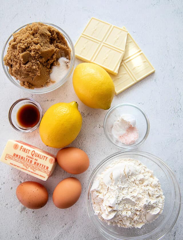 Separate ingredients that go into Lemon Blondies with White Chocolate, from top left and clockwise- Brown and granulated sugar, white chocolate, baking powder, salt, cream of tartar, flour, eggs, butter, vanilla and lemon extracts, lemons.