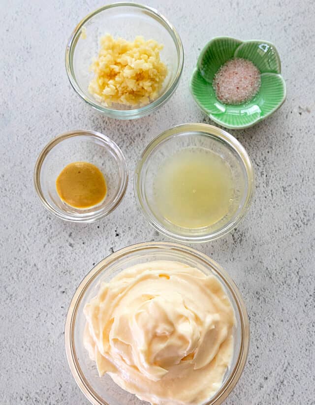 Ingredients in garlic aioli. From top left and moving clockwise: minced garlic, salt, lemon juice, mayonnaise, Dijon mustard.