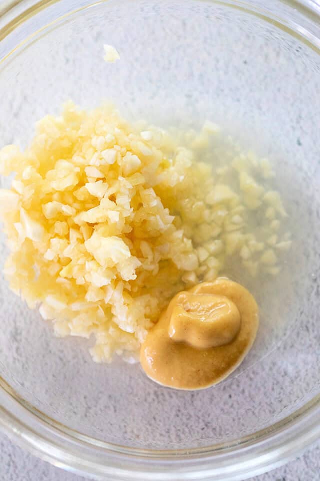 Minced garlic, lemon juice, and Dijon mustard in a clear bowl.