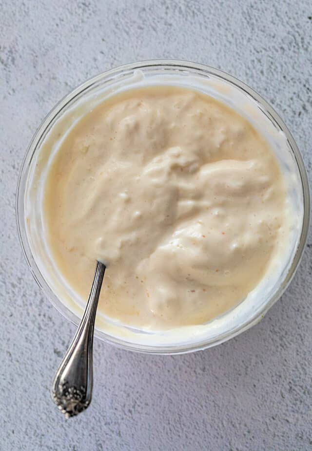 Closeup of garlic aioli in a bowl with a spoon in the aioli.